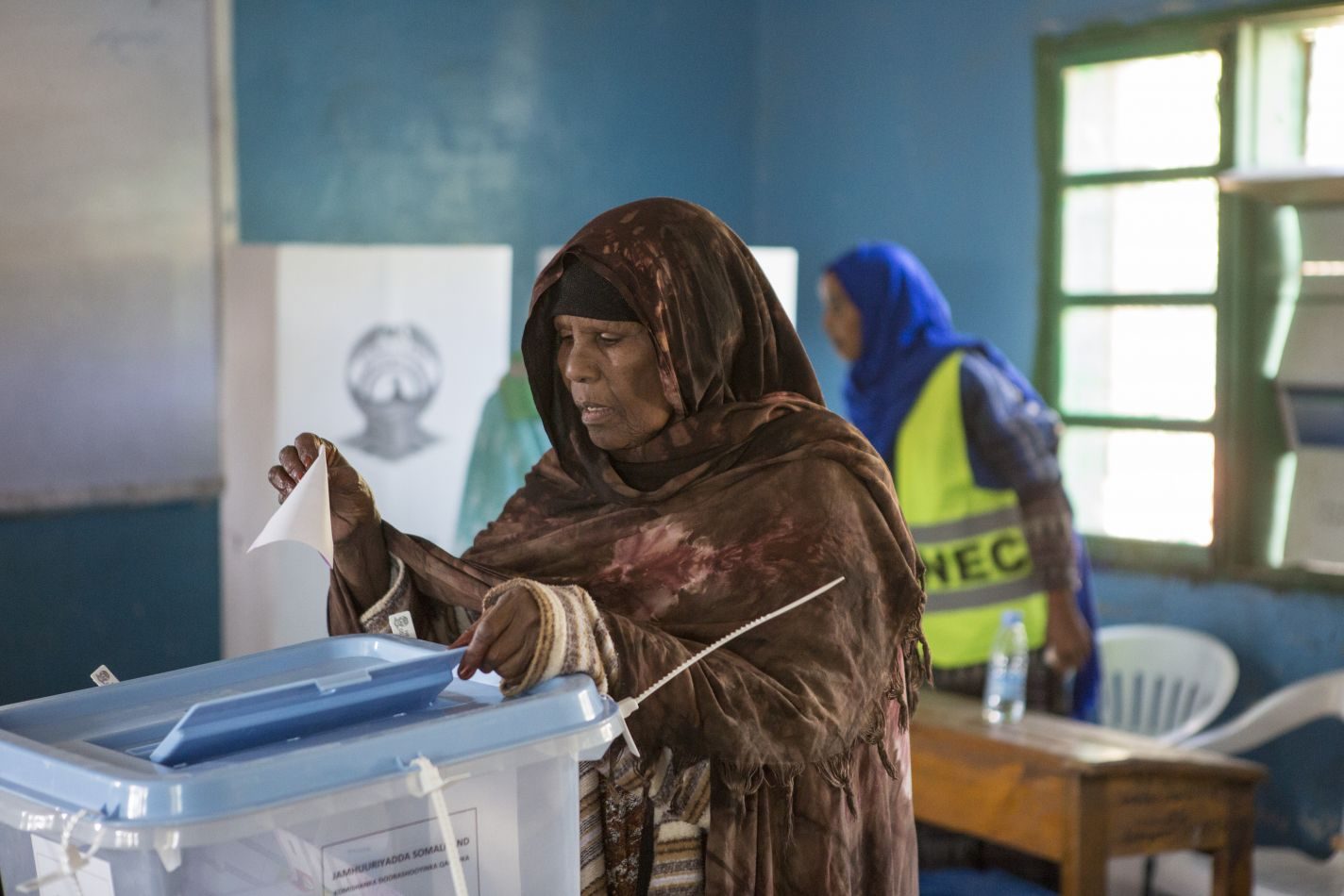 A voter places her ballot into a sealed transparent box